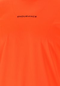 Ljus orange atletisk skjorta i texturerad tyg, med rund halsringning och ordet "ENDURANCE" i svart text på framsidan.