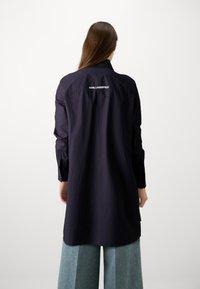 Marineblaue Langarmbluse mit Kragen und geknöpften Manschetten, auf deren Rückseite "KARL LAGERFELD" gestickt ist. Glattes Material mit lockerer Passform.