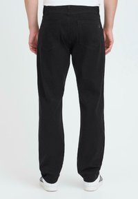 Zwarte denim broek met een rechte snit, twee achterzakken en een standaard tailleband. Gecombineerd met witte sneakers met blauwe strepen.