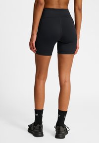 Czarne spodenki sportowe z wysokim stanem, gładką fakturą i minimalnymi szwami. Noszone z czarnymi skarpetkami do kostek i butami sportowymi.
