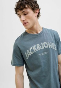 Mørk teal bomulds t-shirt med "JACK & JONES" logo i stor hvid slidt skrifttype, korte ærmer og klassisk rund halsudskæring.