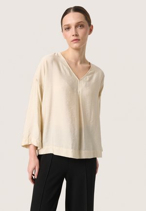 Blusa leggera color crema con scollatura a V, spalle scese e maniche a tre quarti. Tessuto morbido e vestibilità rilassata.