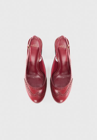 Red leather slingback shoes featuring a brogue design, smooth texture, almond-shaped toe, and a gold-tone buckle accent.