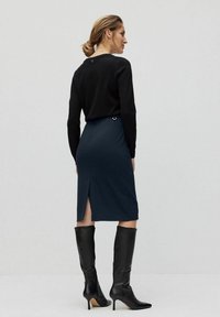 Marinblå pennkjol med sprund bak, i kombination med en svart långärmad topp. Funktioner inkluderar en figurnära design och metallisk detalj vid halsringningen.