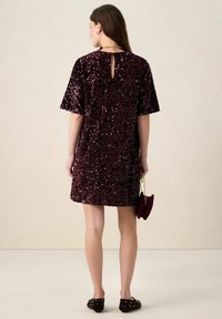 Robe bordeaux à sequins avec manches courtes, dos à découpes, coupe décontractée, associée à un petit sac et des chaussures ornées de clous.
