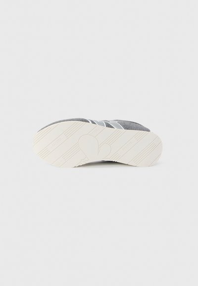 Sole of gray sneaker with white rubber bottom and patterned tread, photographed against a plain light background.