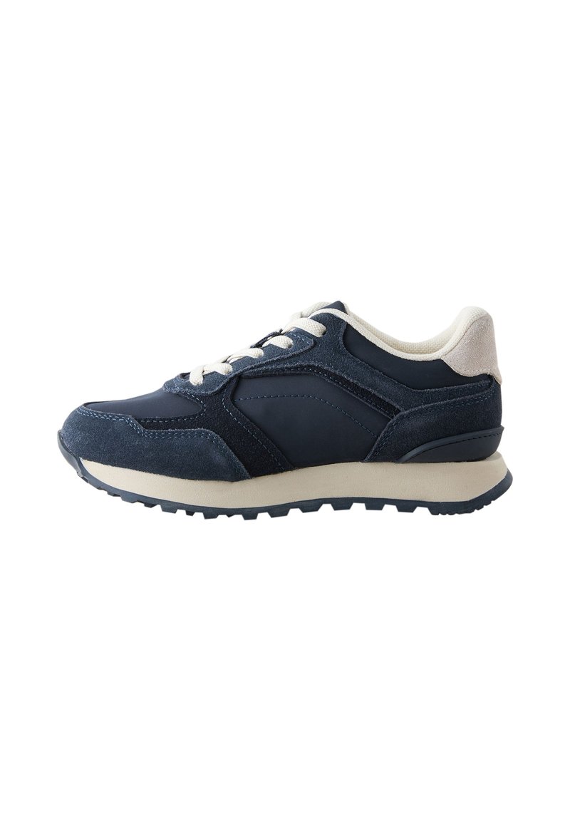 Chaussure de sport bleu marine composée d'un mélange de suède et de matériaux synthétiques, semelle plate beige, design à lacets et accents texturés subtils.