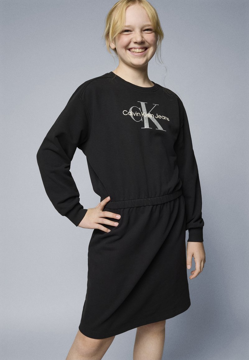 Vestido de sweatshirt preto com mangas longas, cintura elástica e logótipo Calvin Klein Jeans em prata. Textura suave e corte até ao joelho.