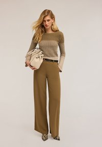 Pulover tricotat bej cu model zigzag, pantaloni largi oliu și o poșetă crem cu fundă. Pantofii cu toc ascuțit cu imprimeu de șarpe completează ținuta.