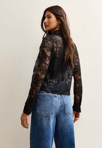 Czarny top z długim rękawem z koronką, z teksturowanym wzorem i subtelnymi cekinami. Zestawiony z dżinsami w kolorze niebieskim o wysokim stanie.