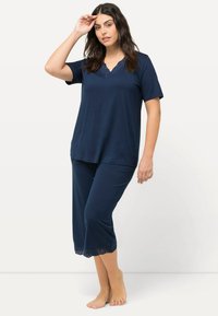 Ensemble de loungewear bleu marine en tissu doux. Haut à manches courtes avec un col en V, présentant des détails en dentelle. Pantalons cropped avec un ourlet découpé au laser.