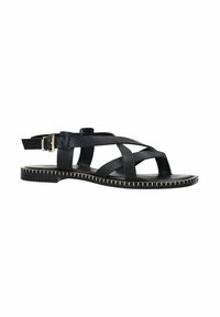 Sandale en cuir noir avec des brides croisées, fermeture à boucle et semelle plate ornée de surpiqûres dorées le long du bord.