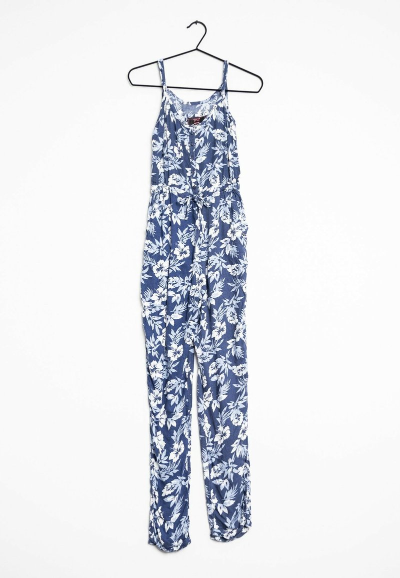 Combinaison bleue sans manches avec imprimé floral blanc accrochée à un cintre noir sur fond blanc.