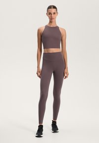 Luxusný športový súprava v tlmených fialových odtieňoch, ktorá obsahuje krátky top s vysokým golierom a legíny s vysokým pásom, oboje vyrobené z hladkého a pružného materiálu.