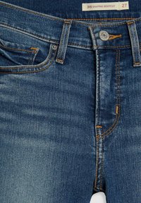 Blaue Jeans aus Denim mit Bootcut-Design, ausgestattet mit orangenen Nähten, einem Frontknopfverschluss und ausgebleichten, abgetragenen Effekten im Oberschenkelbereich.