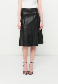 Black pleated leather skirt with a smooth finish, reaching mid-calf length, paired with strappy black high-heeled sandals.