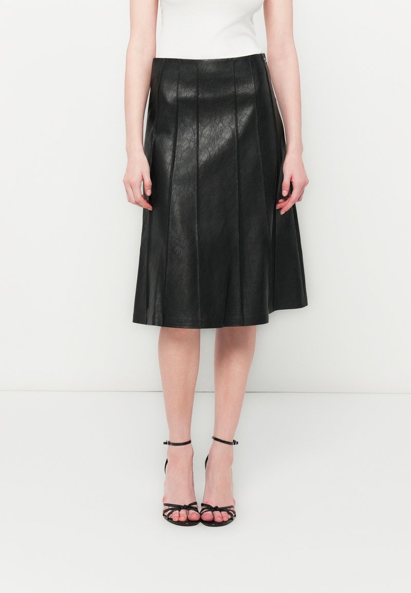 Black pleated leather skirt with a smooth finish, reaching mid-calf length, paired with strappy black high-heeled sandals.