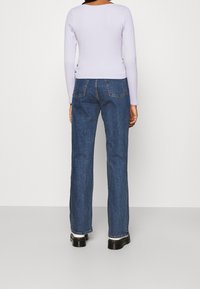 Ljust lila långärmad topp med rundad ryggkrage, ihop med högmidjade raka mörkblå jeans. Svarta platåstövlar.