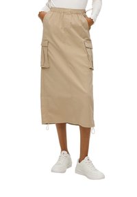 Beige cargorok met een elastische tailleband, zijzakken, rechte snit en trekkoorddetails. Gepaard met witte sneakers.