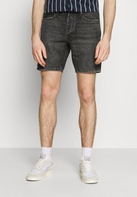 Shorts de mezclilla negros con diseño de cinco bolsillos, textura desgastada y dobladillo deshilachado. Combinados con zapatillas blancas y una camisa de rayas en azul marino.