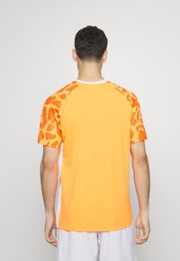 Camiseta deportiva naranja de manga corta, con un patrón de formas abstractas en un tono más oscuro de naranja en los hombros.