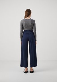 Grå ribbad figurnära långärmad topp kombinerad med marinblå vida byxor med resår i midjan. Svartvita accent skor.