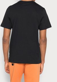 Schwarzes Baumwoll-T-Shirt mit kurzen Ärmeln, rundem Halsausschnitt und glatter Textur. Es verfügt über ein kleines Logodetail nahe dem Saum.