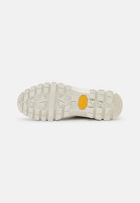 Suela de zapatilla blanca con un patrón de dibujo robusto, que presenta un prominente logo amarillo y varios segmentos texturizados para mejorar el agarre.