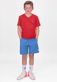 Rotes V-Ausschnitt-T-Shirt, blaue Sportshorts, weiße Socken und Turnschuhe. Das T-Shirt hat ein kleines Logo; die Shorts verfügen über eine Design mit Seitentaschen.