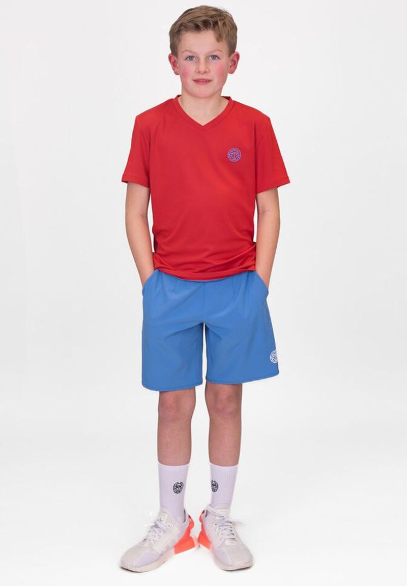 Rotes V-Ausschnitt-T-Shirt, blaue Sportshorts, weiße Socken und Turnschuhe. Das T-Shirt hat ein kleines Logo; die Shorts verfügen über eine Design mit Seitentaschen.