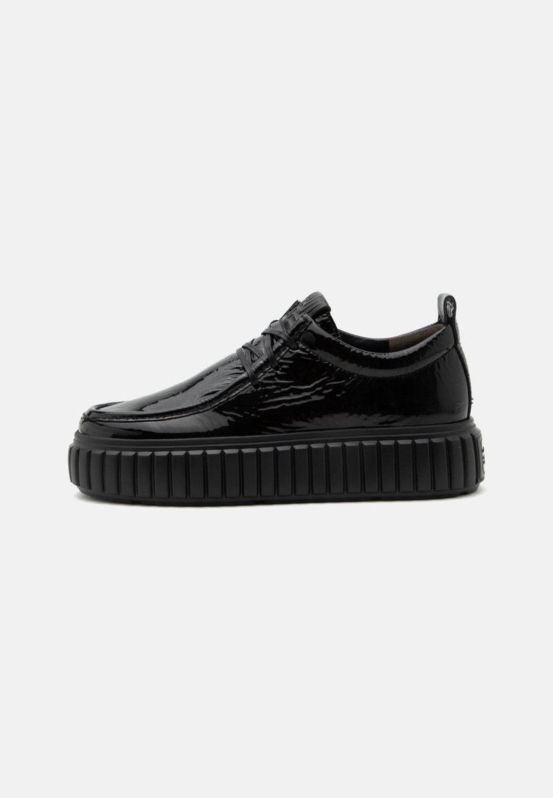 Chaussure basse noire brillante avec semelle plateforme épaisse et texturée et lacets à l'avant, vue de côté sur fond uni.