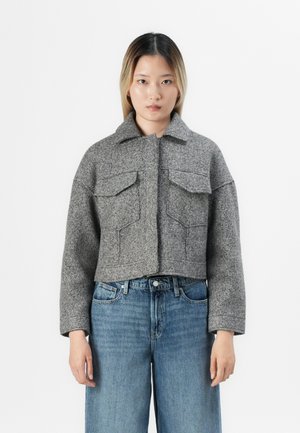 Gray wool cropped jacket with a pointed collar, two chest pockets, and textured fabric. Paired with high-waisted blue denim jeans.