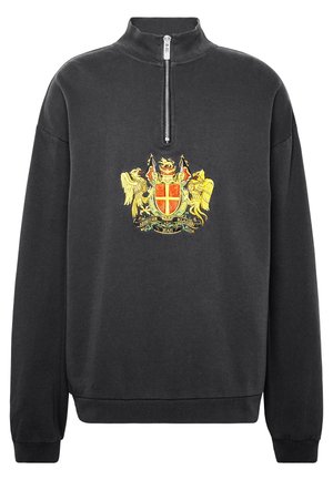 Musta neljännesvetoketjullinen collegepaita, jossa on korkea kaulus ja rintakehän keskellä keltainen ja punainen kirjailtu heraldinen vaakuna.