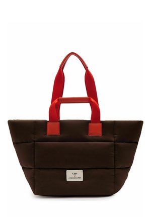Braune gesteppte Tragetasche mit leuchtend roten Griffen, vorne mit einem kleinen weißen Etikett mit dem Text "UNIO x LES VISIONNAIRES".