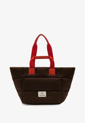 Brown quilted tote bag with bright red handles, featuring a small white label with "UNIO x LES VISIONNAIRES" text on the front.