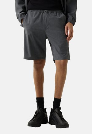 Mørkegrå knælange shorts til mænd med elastisk linning og sidelomme, kombineret med sorte sokker og sorte sportssko.