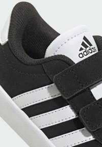 Černo-bílé sportovní boty vyrobené z semišových a syntetických materiálů, s na suchý zip a třemi bílými pruhy na boku.