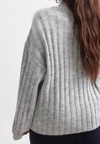 Grau gestreifter Strickpullover mit hohem Kragen und überschnittenen Schultern, der eine weiche Textur und eine lockere Passform aufweist, von hinten gesehen.