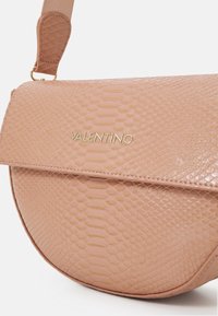 Rosa fuskormsläder crossbody-väska med böjd form, magnetisk lockstängning och präglad logotyp i guld. Justerbar rem ingår.