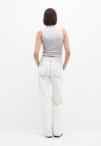 Graues, ärmelloses Oberteil mit taillierter Passform, kombiniert mit weißen, weit geschnittenen Jeans, die ein strukturiertes Muster und verblasste blaue Akzente aufweisen.