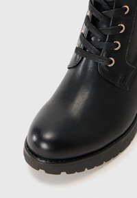 Black leather ankle boot with a rounded toe, textured upper, and metallic eyelets for laces. Rubber sole with a tread pattern.