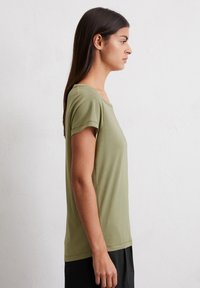 Olivengrünes T-Shirt mit kurzen Ärmeln und lässiger Passform, Rundhalsausschnitt, weicher Textur und seitlicher Nahtdetails, kombiniert mit dunklen Hosen.