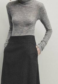 Maglione a collo alto grigio in tessuto morbido e elastico, abbinato a una lunga gonna grigia scura con tasche laterali e un design liscio e sartoriale.