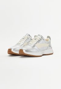 Silberne, metallische Sneakers mit cremefarbenen Akzenten, strukturiertem Obermaterial und einer weißen Zwischensohle, die eine Gummirubber-Zickzack-Laufsohle aufweisen.