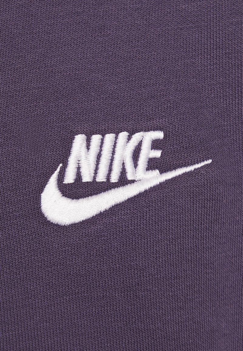 Logo Nike blanc brodé sur un fond en tissu tricoté violet.