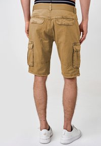Khaki cargo šorts s teksturiranom tkaninom, s dva velika bočna džepa, petljama za remen i prevrnutim rubom. Nositi s bijelim tenisicama.