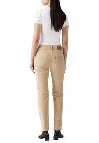 Jeans beiges ajustés avec poches arrière, patch en cuir sur la ceinture, accompagnés d'un haut blanc à manches courtes et de bottes noires à talons.