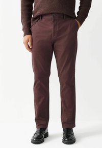 Pantaloni bordeaux cu o textură netedă, croială dreaptă, buzunare frontale și închidere cu buton, asortați cu pantofi din piele negri.