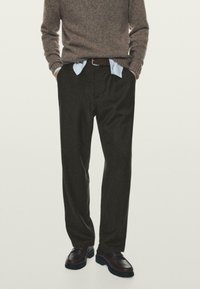 Šedé vlněné kalhoty s volným střihem, doplněné o světle modrou košili a hnědé kožené boty. Textura je měkká a strukturovaná.