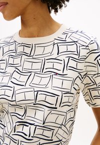 Μπλούζα σε κρεμ χρώμα με κοντά μανίκια και γεωμετρικό σχέδιο σε ναυτικό μπλε. Διαθέτει στρογγυλή λαιμόκοψη και μικρή λογότυπο σε κόκκινο και μπλε στο στήθος.